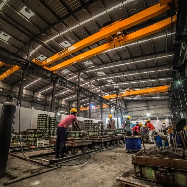 Workers operating an overhead crane inside a steel casting foundry